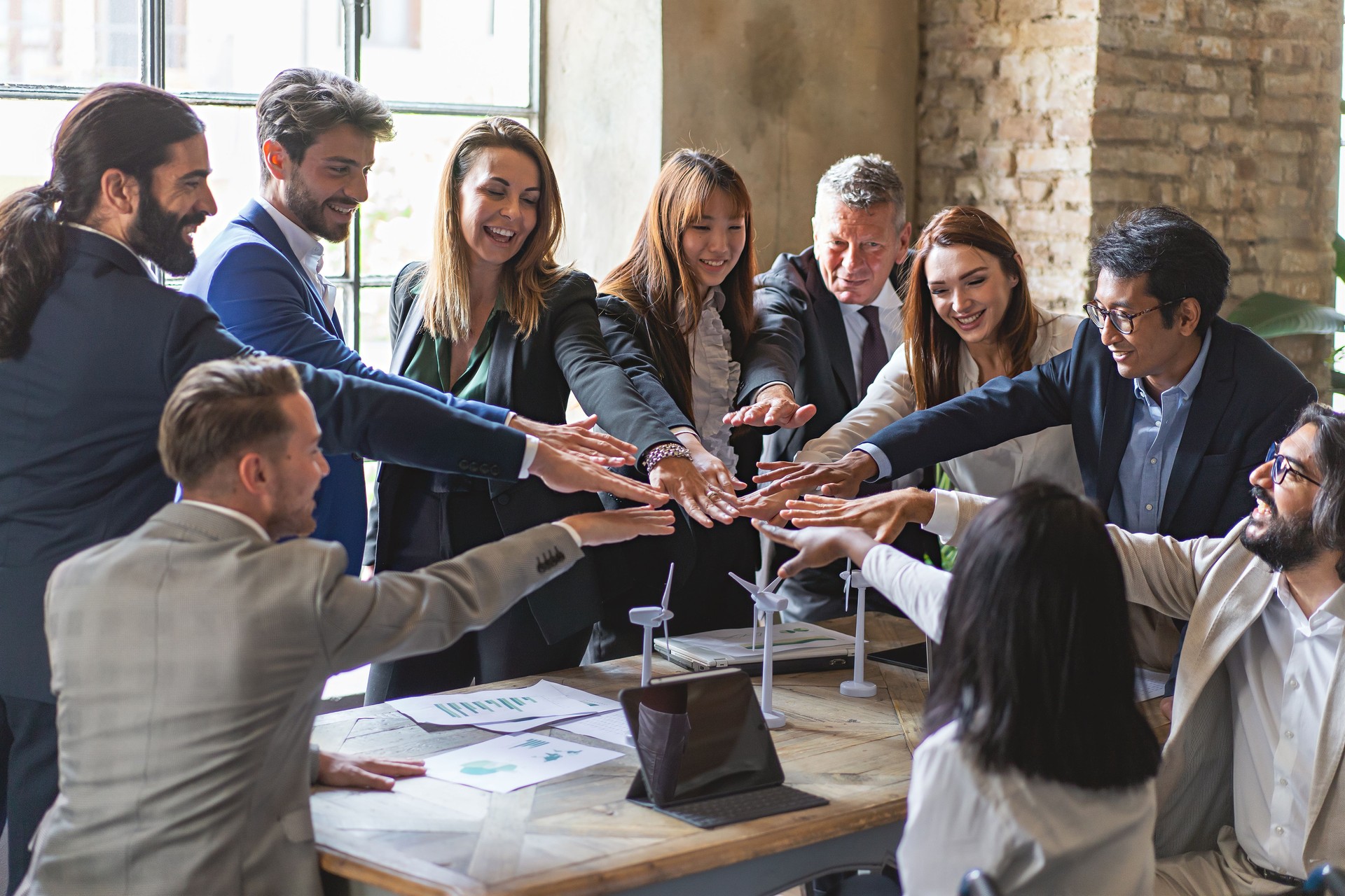 Multiethnic businesspeople joining hands standing around the office desk - Teamwork high five the success of a sustainable project of green economy