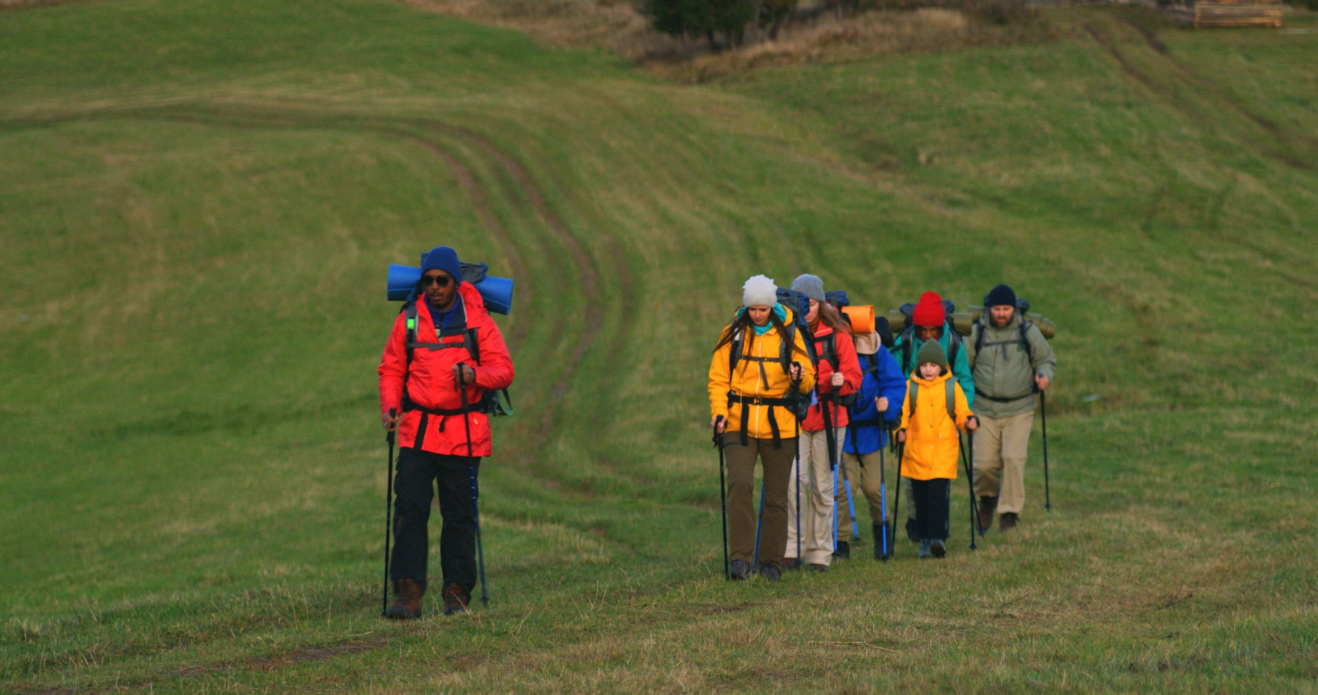 Tourist friends with tracking poles walking along trail on hill