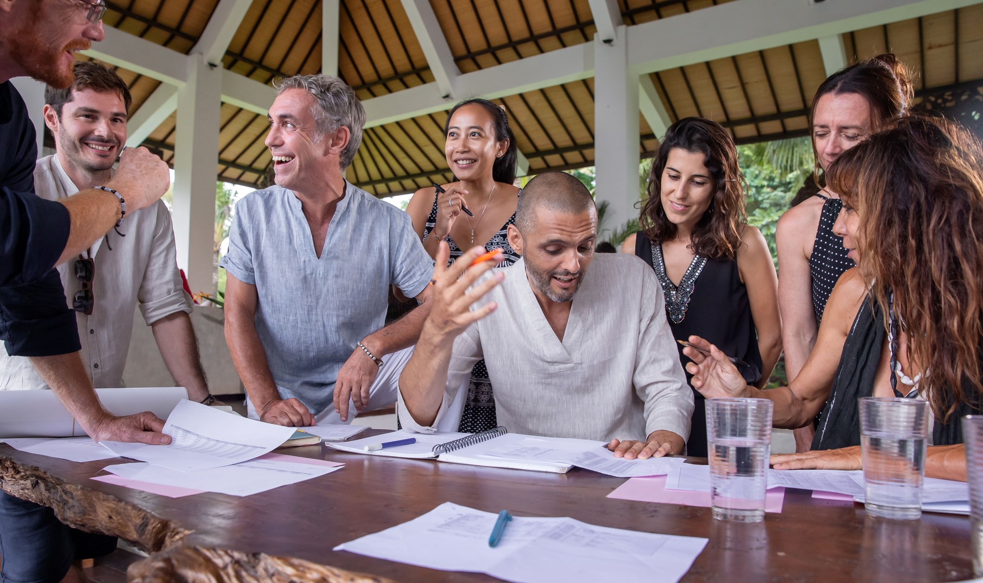 Happy diverse multiethnic business team members talking, discussing and brainstorming on project paperwork at meeting, seminar or presentation outdoor in tropical conference.